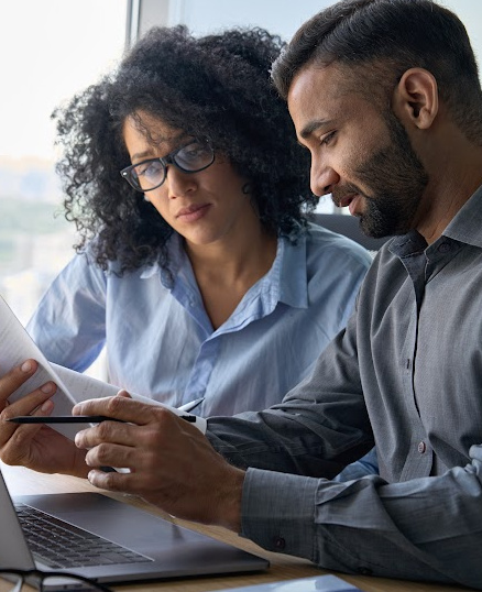 man and woman looking at papers by laptop