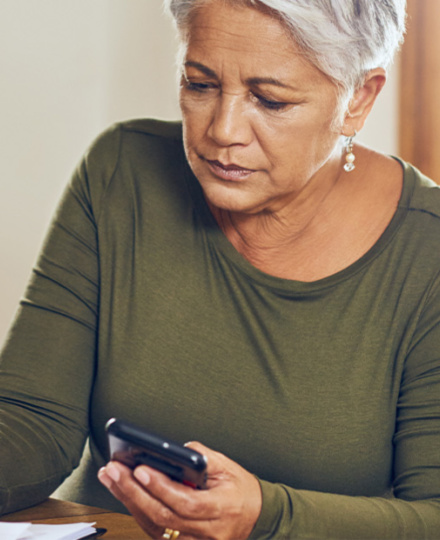 older woman looking at cell phone and bills