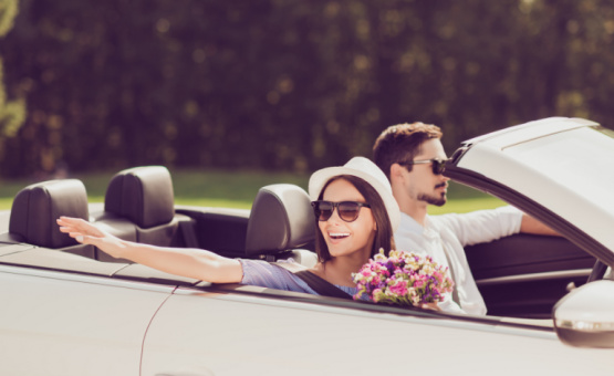 man driving convertible with woman in passenger seat holding flowers