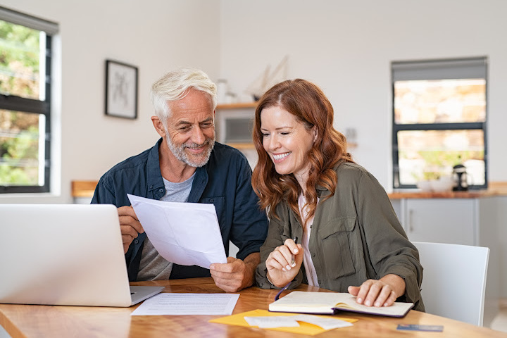 Older man and woman looking at papers near laptop