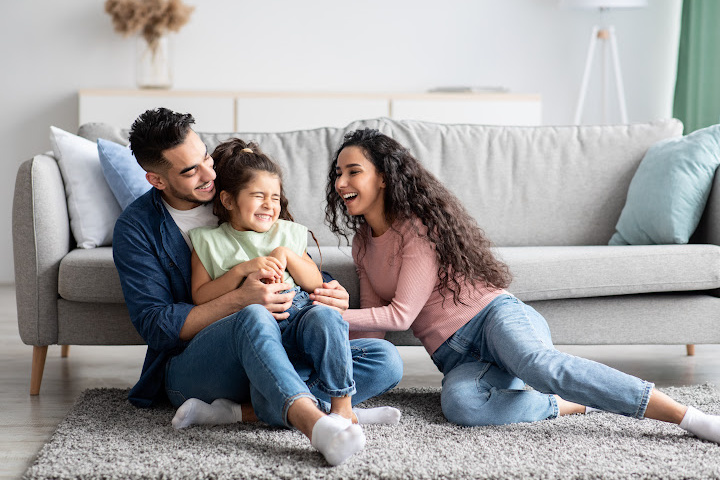 dad, mom, and daughter sitting by couch