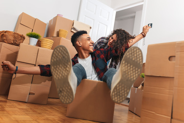 man sitting in moving box looking happily at woman