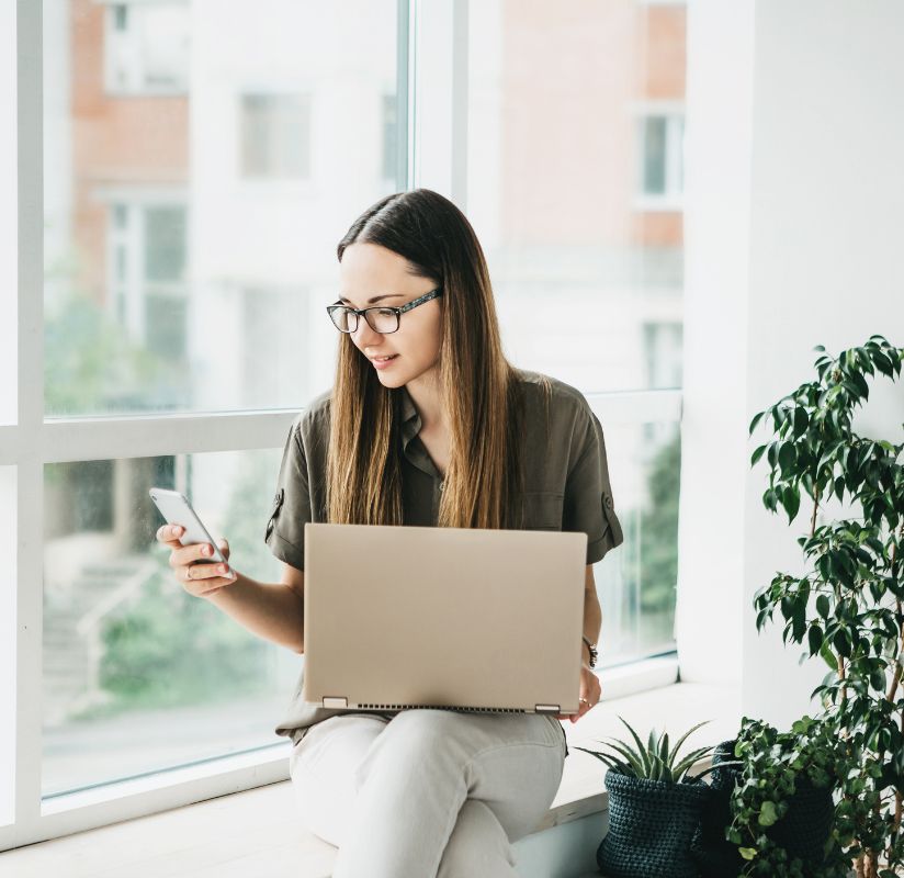 woman looking at cell phone with laptop on lap