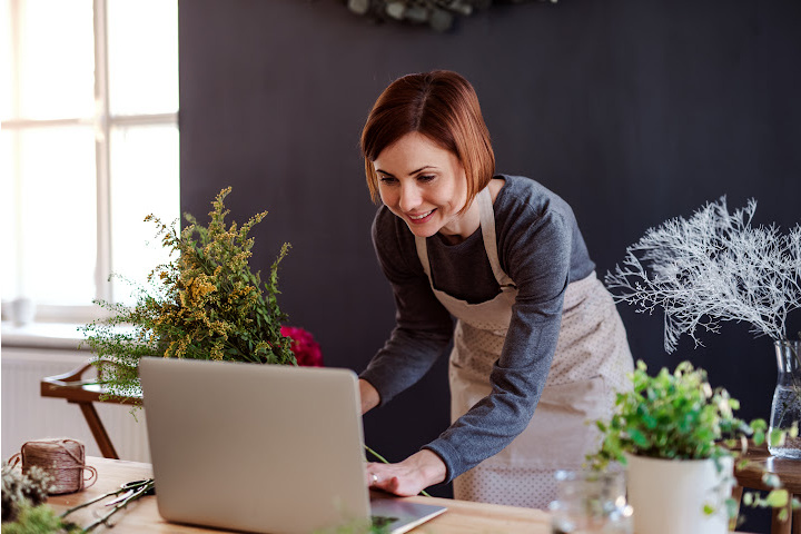 Female florist standing with flowers by laptop